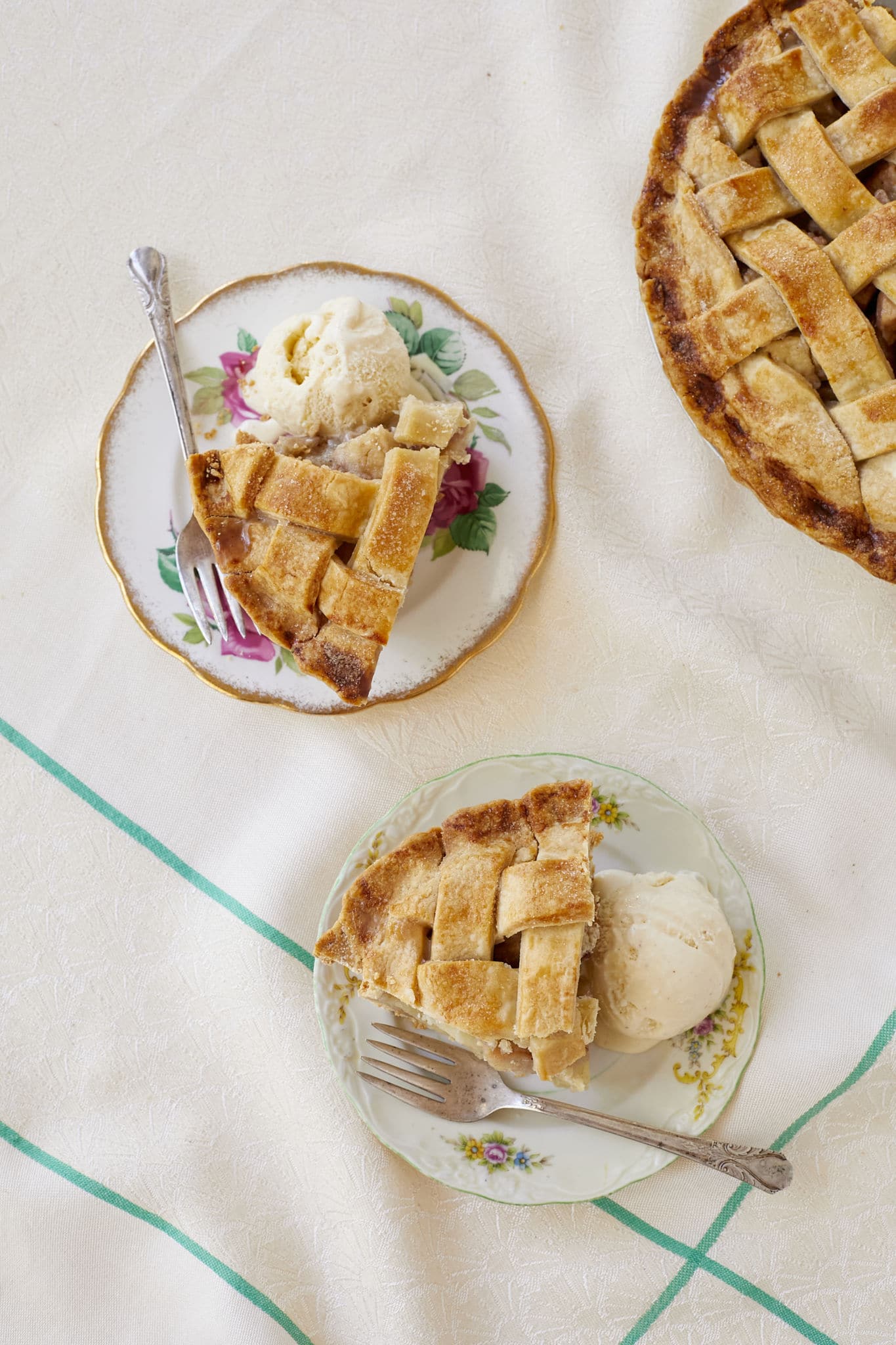 Two slices of pear pie are served with vanilla ice cream on a white table cloth.
