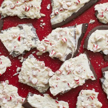 Homemade Chocolate Peppermint Bark, covered in crushed candy canes, are served in pieces on a red table.