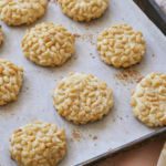 Homemade Pignoli Cookies are displayed on a cookie tray. The almond cookies are covered in pine nuts.