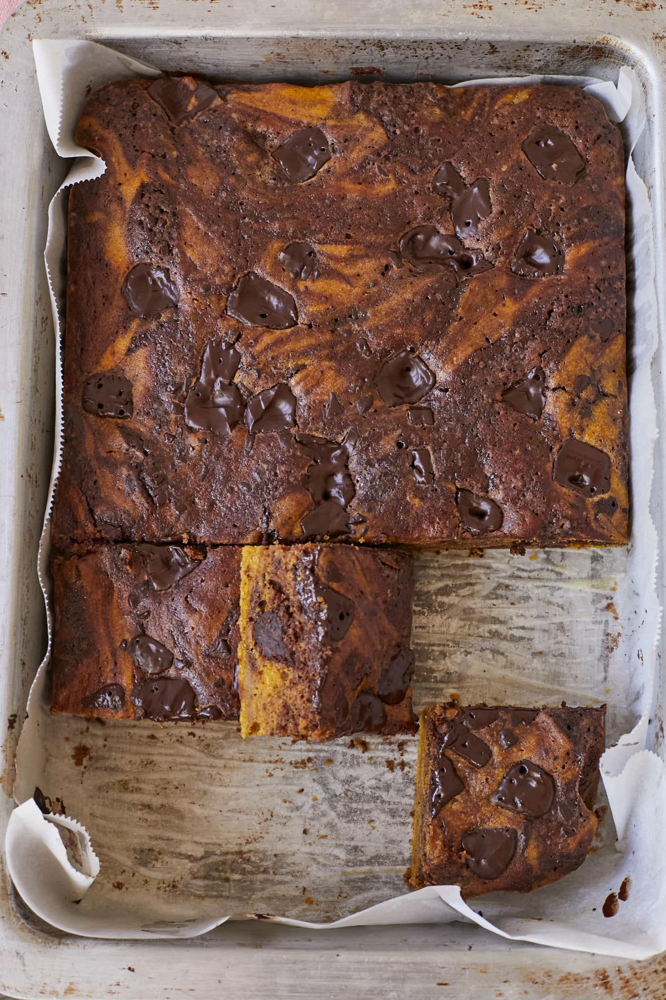 Servings of pumpkin pie brownies are cut from the entire batch with a cross section showing the swirled pumpkin pie.