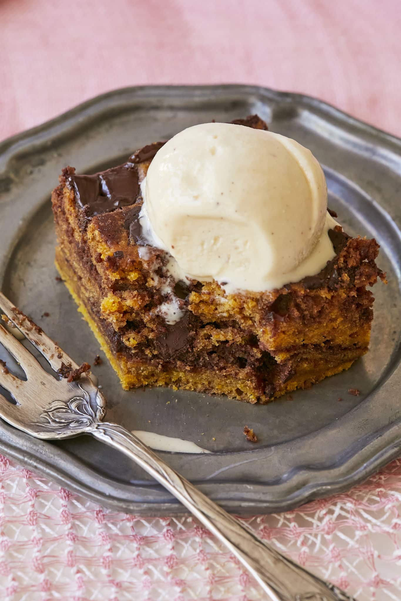 A close-up photo of a pumpkin pie brownie topped with vanilla ice cream. There is a single bite taken from the brownie.