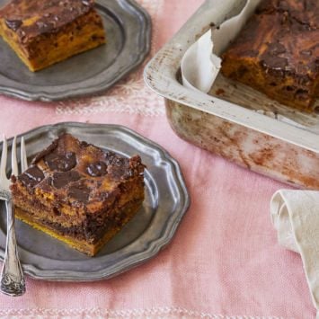 A square slice of homemade pumpkin pie brownies is cut and served on a dish next to the entire batch.