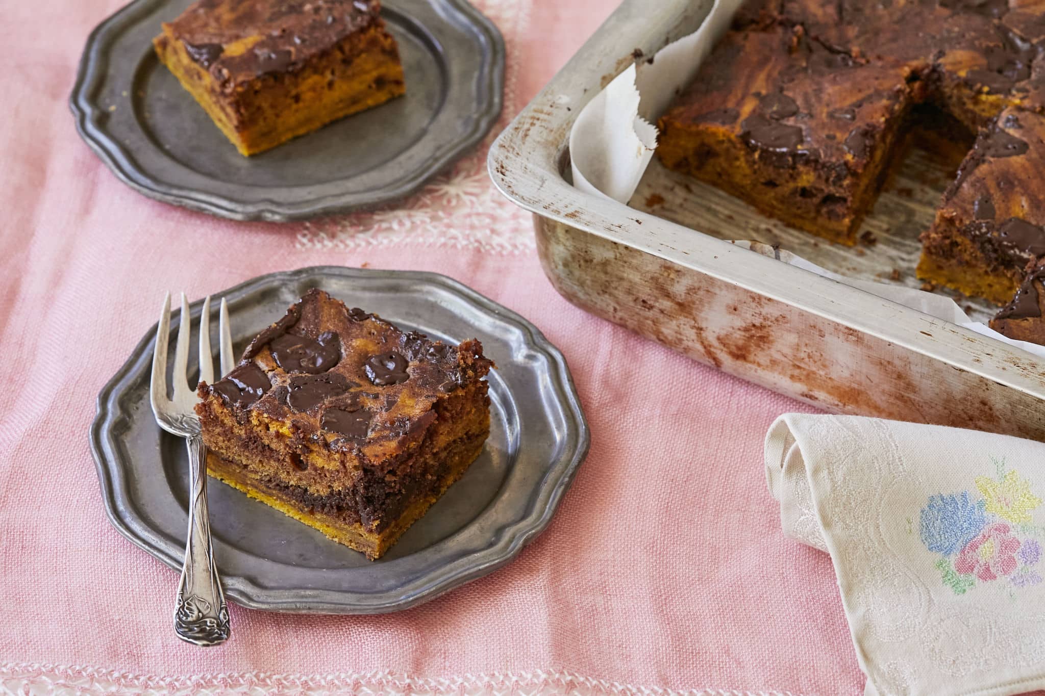 A square slice of homemade pumpkin pie brownies is cut and served on a dish next to the entire batch.