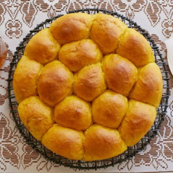 Homemade pumpkin bread rolls are baked in a circular tin. The tops are golden brown and they have risen and cooked to be stuck together.