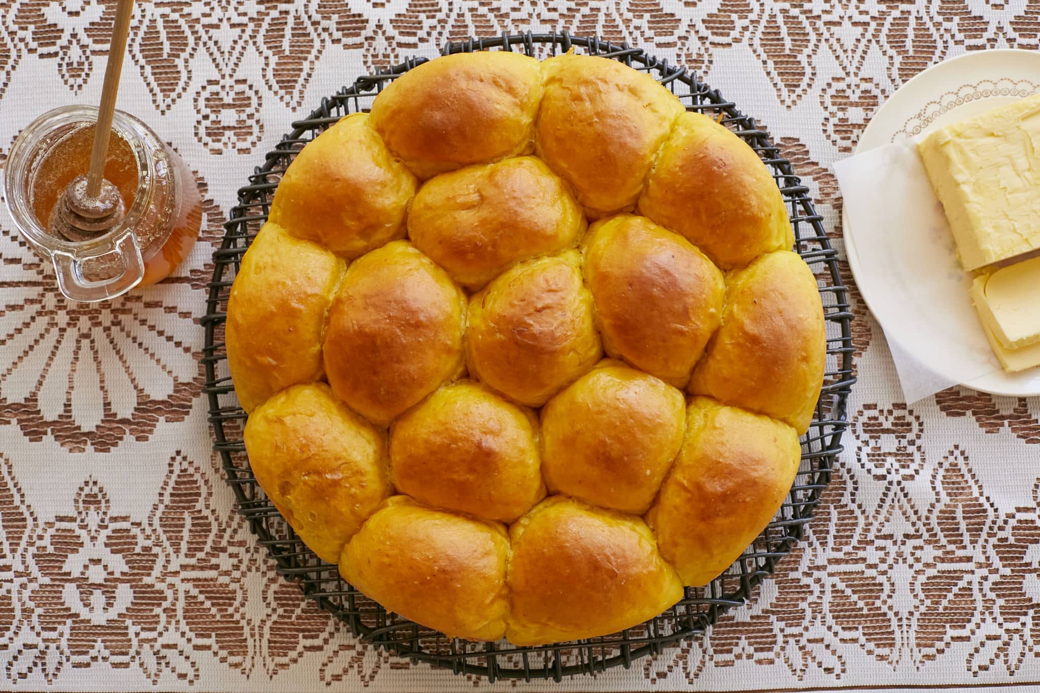 Homemade pumpkin bread rolls are baked in a circular tin. The tops are golden brown and they have risen and cooked to be stuck together.