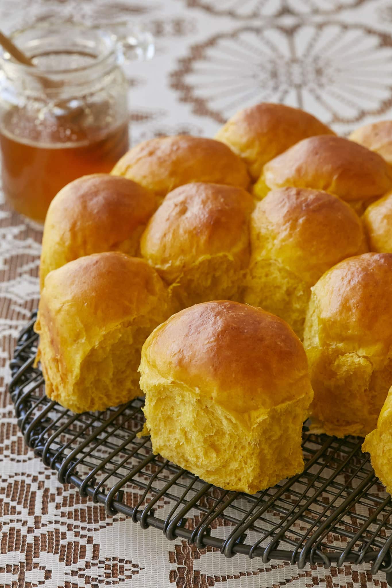 A closeup image of the pumpkin dinner rolls split apart. The soft, fluffy interior of the roll is a pleasant orange color.