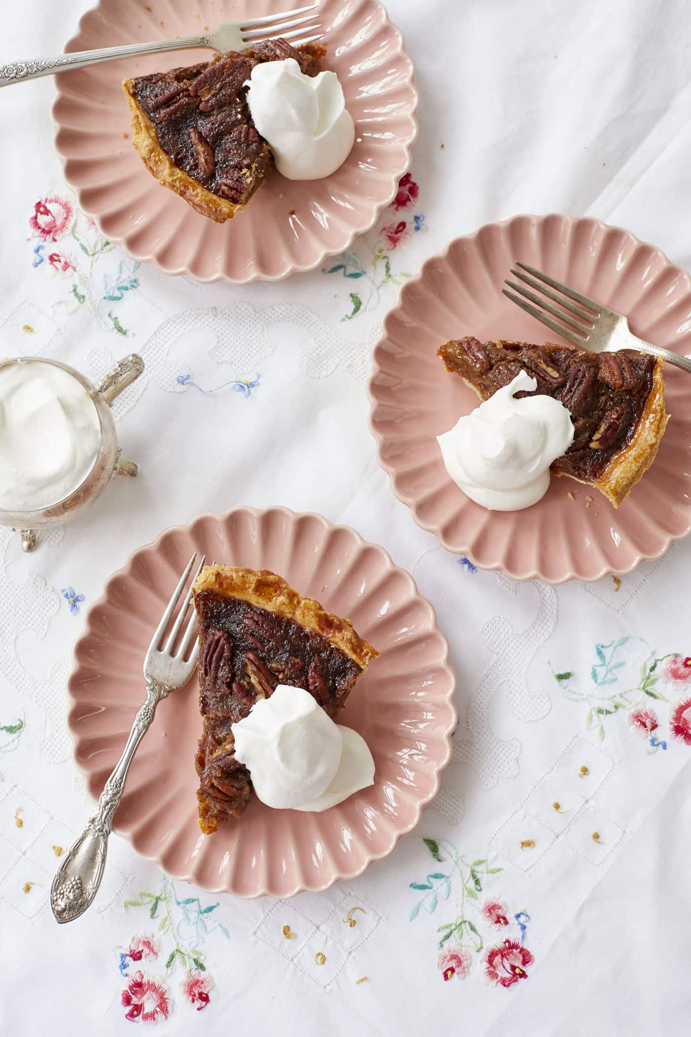 Three slices of pumpkin pecan pie are served on pink dishes with homemade whipped cream.