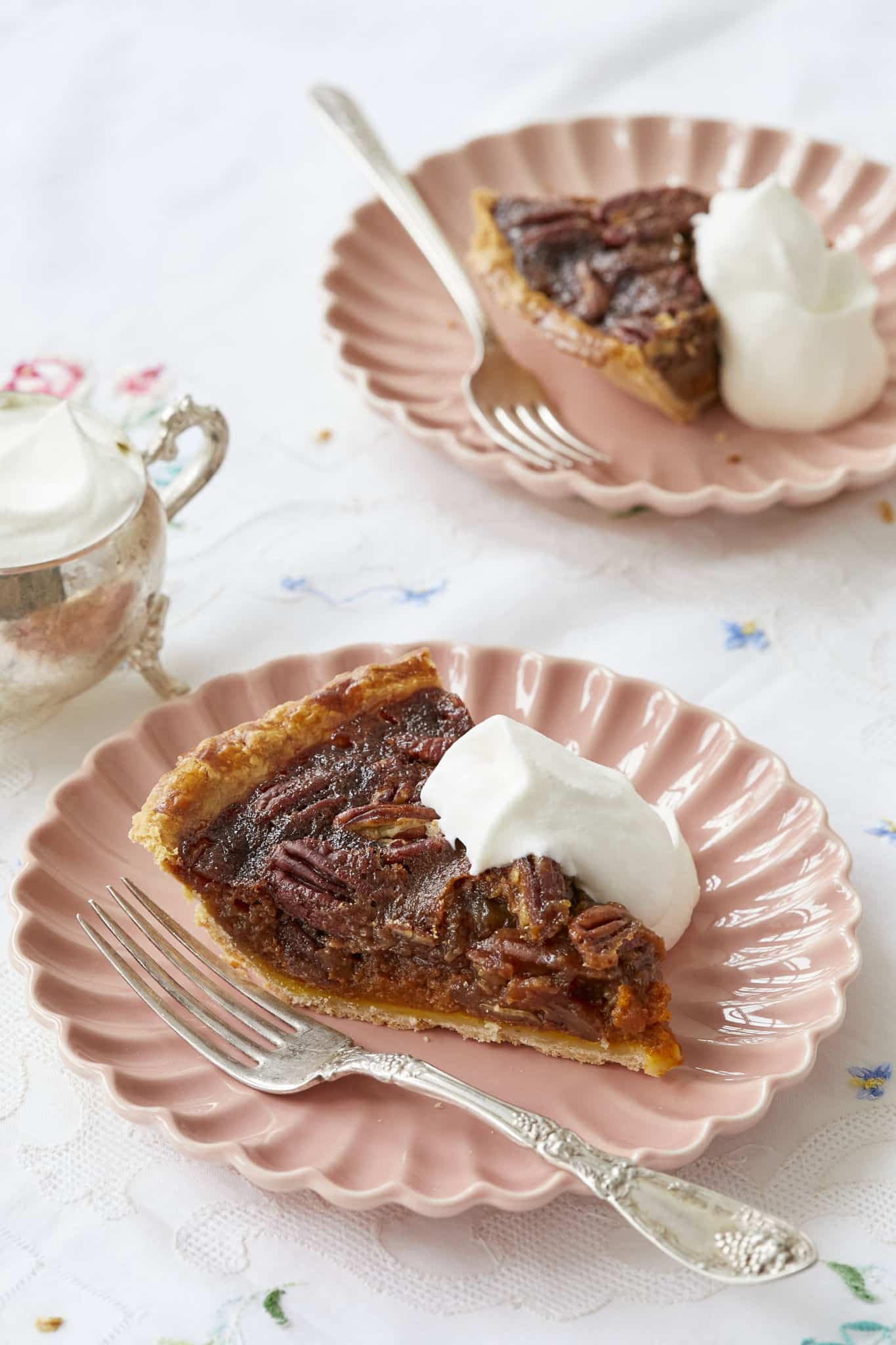 A close-up image of the pumpkin pecan pie shows the pumpkin pie layer underneath the pecan pie top layer. It is topped with fresh whipped cream./
