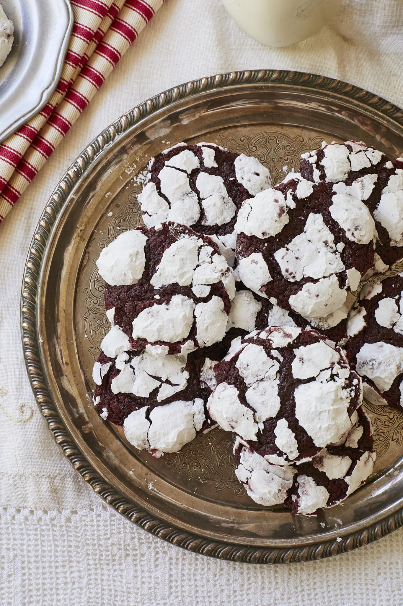 Red Velvet Crinkle Cookies are served on a silver platter. The homemade crinkle cookies have a crackled top and are coated in powdered sugar.