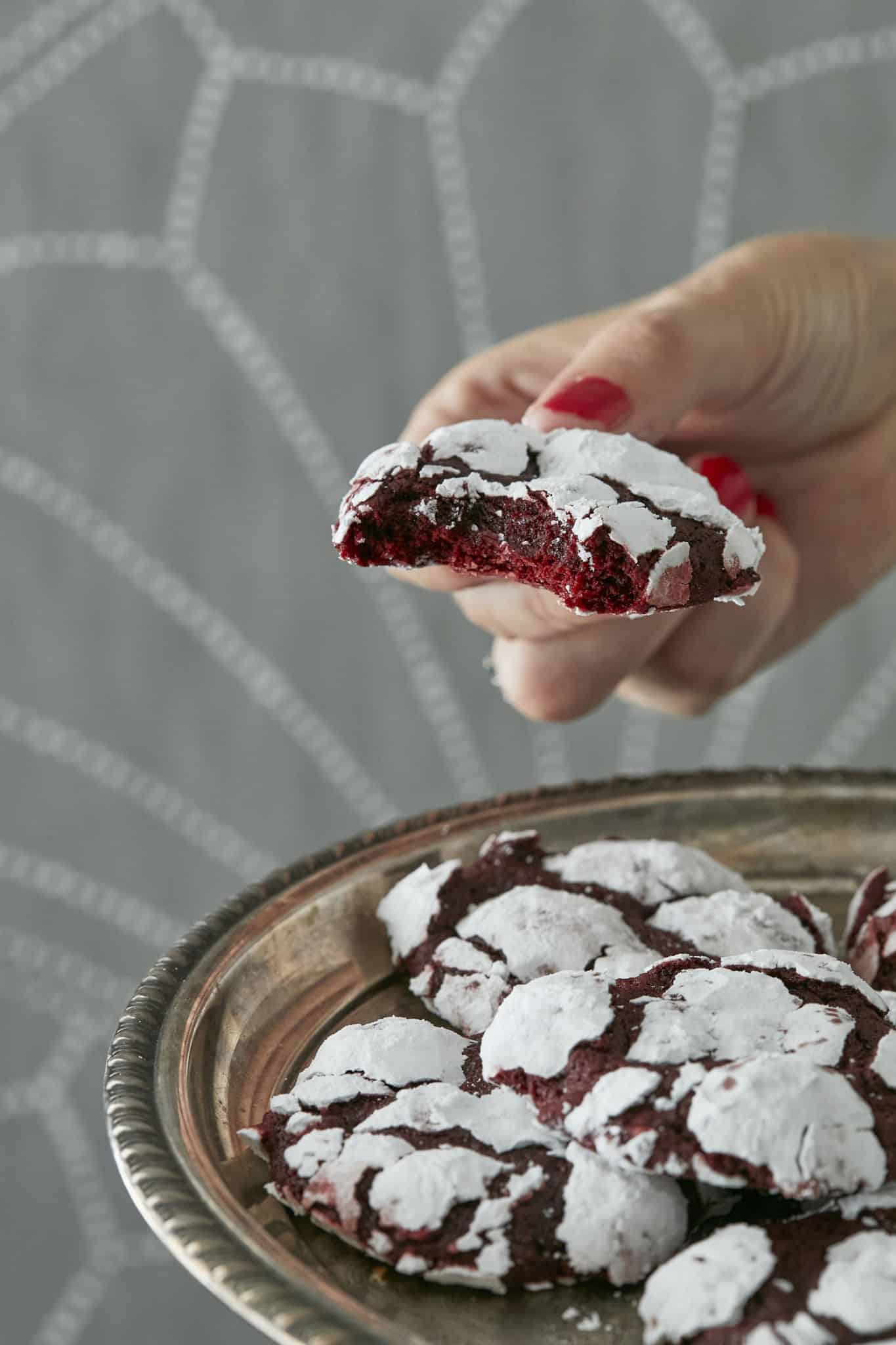 A closeup image of a bite taken out of a Red Velvet Crinkle Cookie shows how moist and chewy the cake-like cookie is, as well as it's iconic powdered sugar coating.