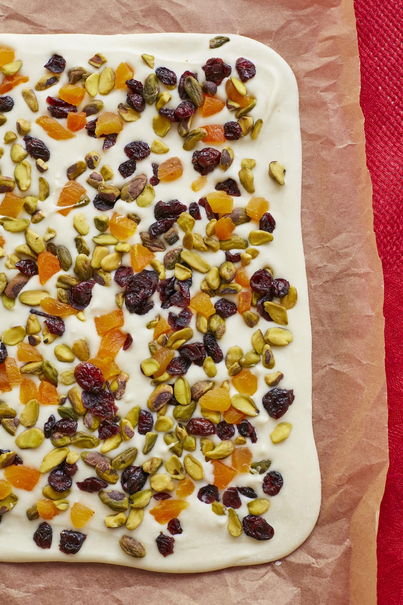 Cranberry White Chocolate Bark, with pistachios and dried apricot, is spread into a thin layer on top of parchment paper.