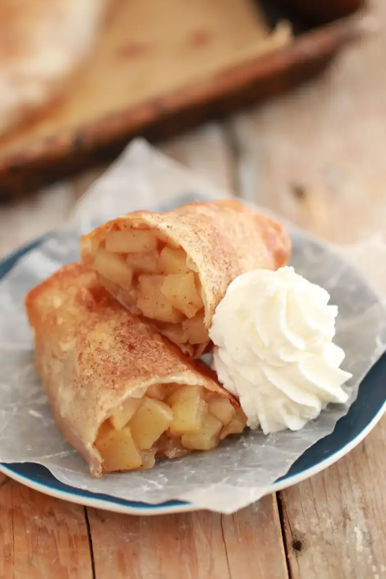 Apple pie filling is baked into an egg roll shell and topped with cinnamon, served with whipped cream.