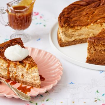 A slice of caramel apple cheesecake was cut for the whole cake and served with whipped cream on top with caramel sauce on the side.