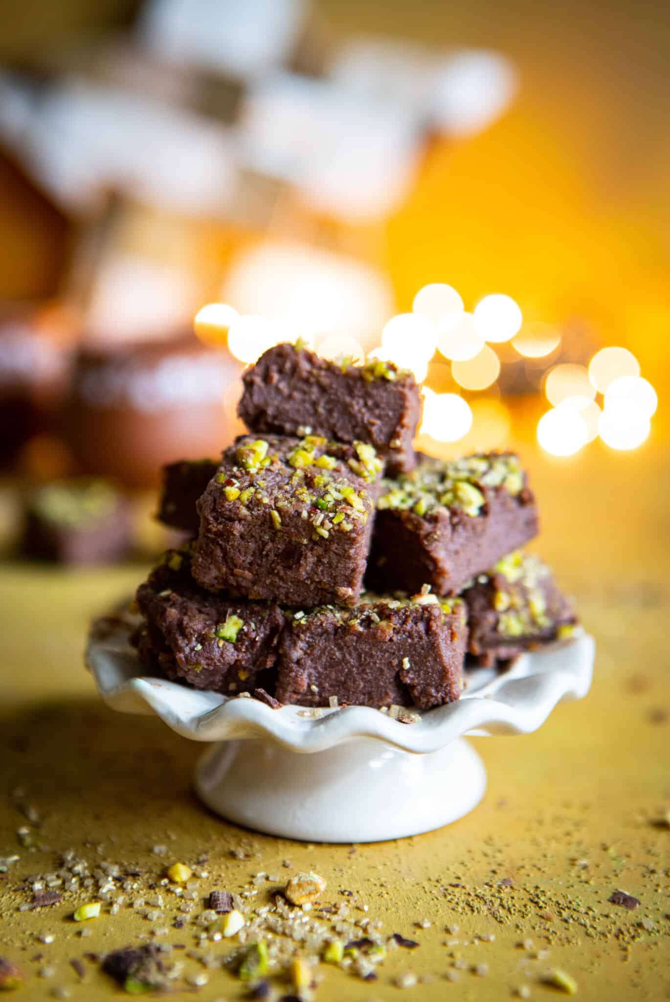Finished chocolate kalakand sprinkled with chopped pistachios stacked on a white serving platter.