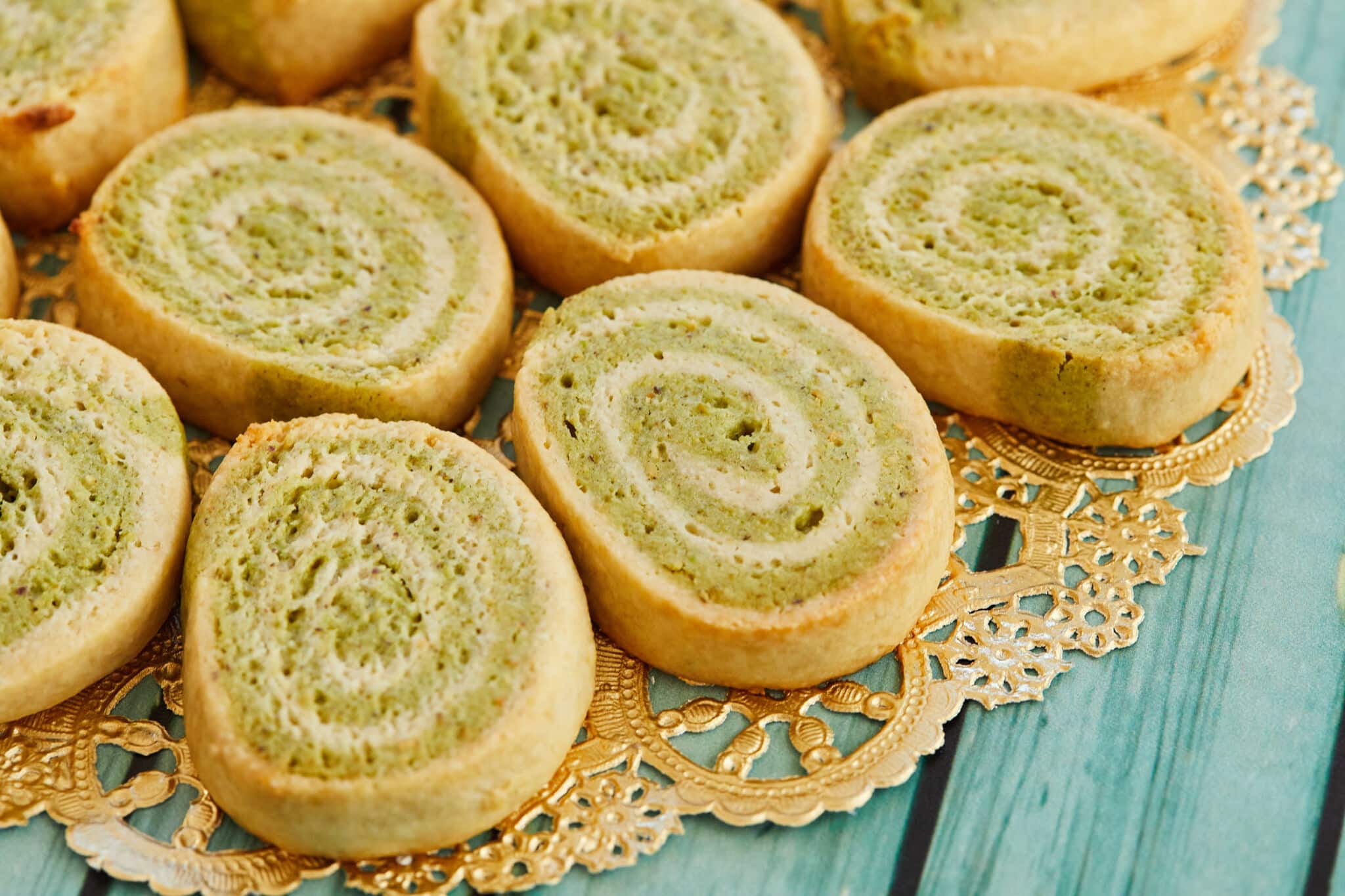 A plate of colorful kaju pista rolls on a gold doily laid out on a wooden table.