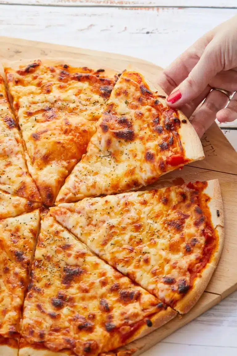 Homemade pizza is served on a wooden cutting board, cut into slices. The crust is golden brown with melted cheese on top.