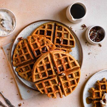 Three homemade pumpkin waffles are served on a plate next to a cup of coffee.