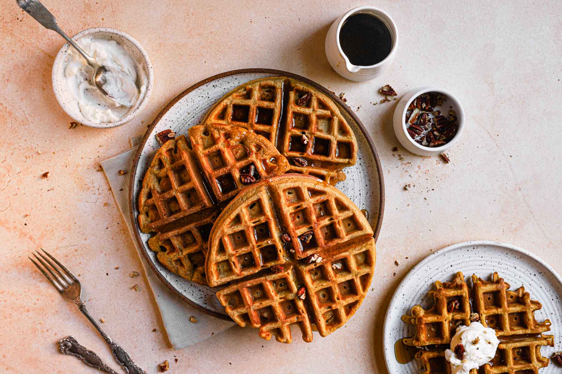 Three homemade pumpkin waffles are served on a plate next to a cup of coffee.