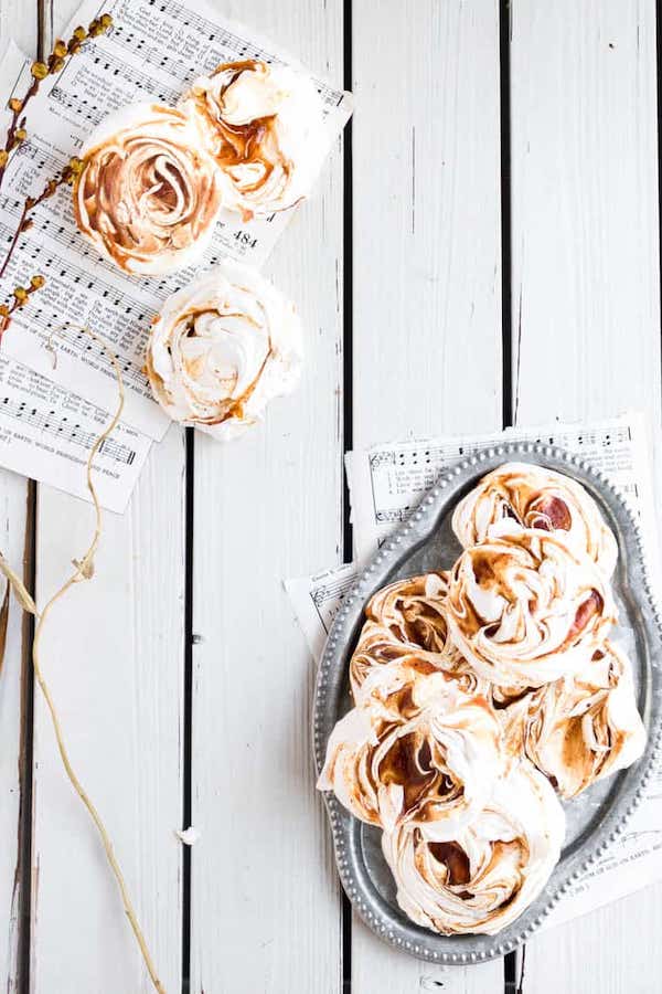 Pumpkin meringues laid out on a silver platter and sheets of music acting as tablecloths on a white wooden table. 