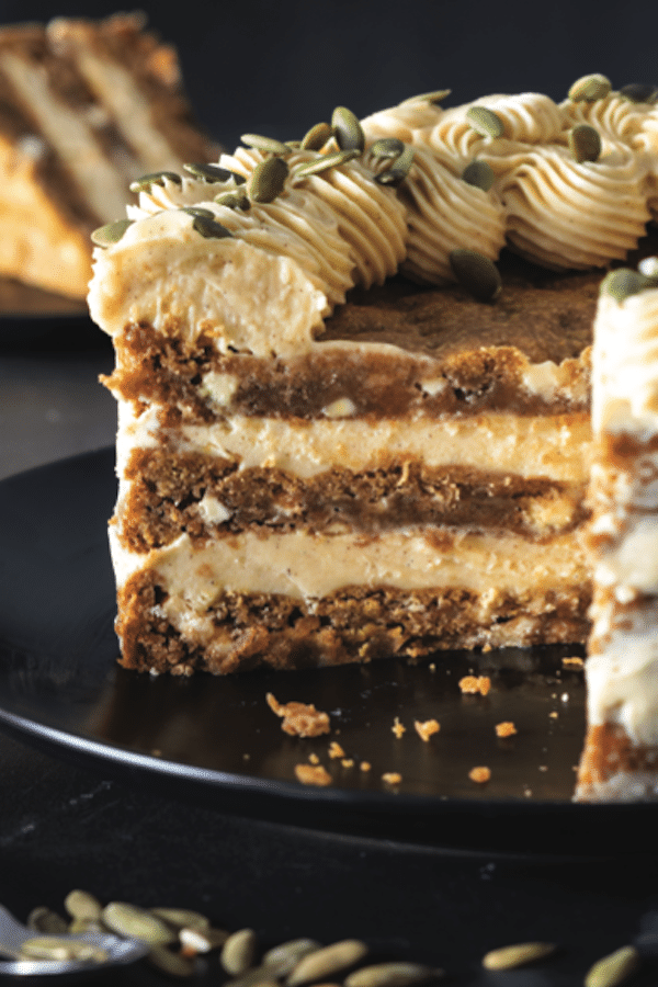 A cake with a slice cut out, so you can see the beautiful layers, on a plate with pumpkin seeds as garnish.