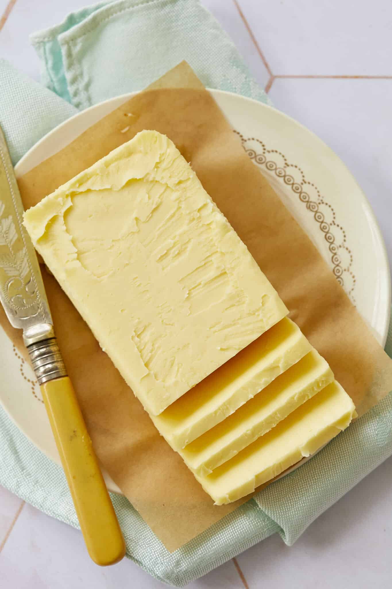 A block of butter is on a parchment paper-lined plate with a butte knife on the left. 