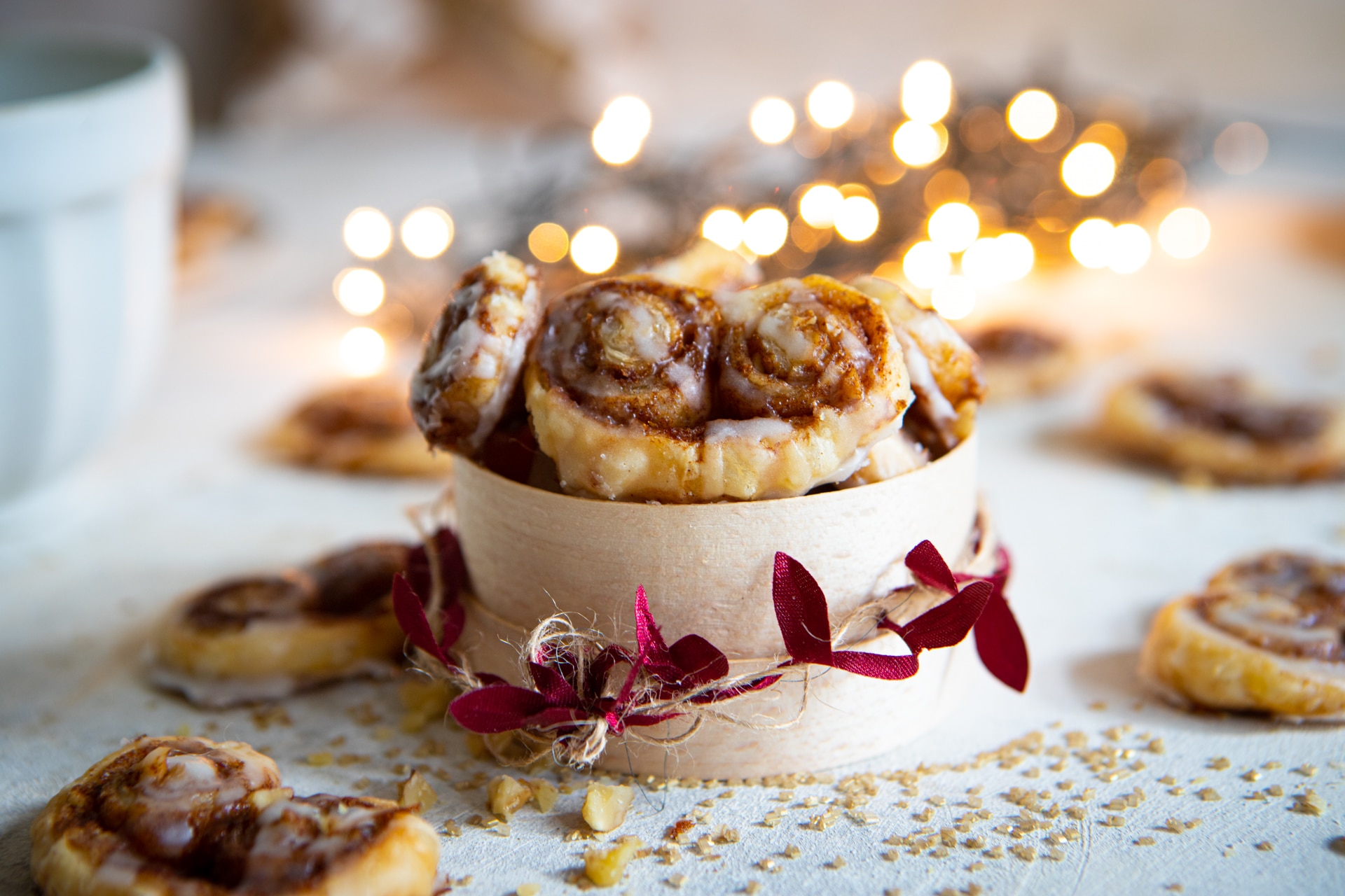 A festive tub of baked cinnamon roll palmiers with a few individual palmiers laid out and lights in the background.