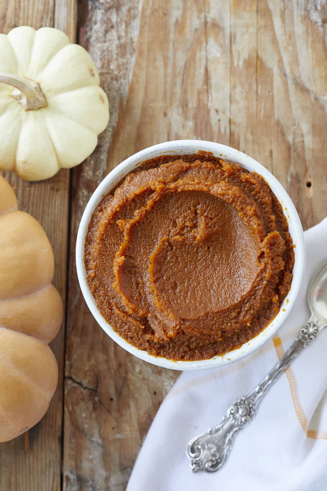 Creamy, spice homemade pumpkin butter is served in a white bowl next to two small squashes. 