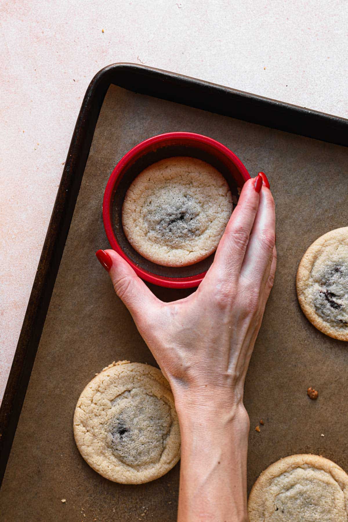 Dee uses a circular cookie cutter to help round the just-baked cookies. 