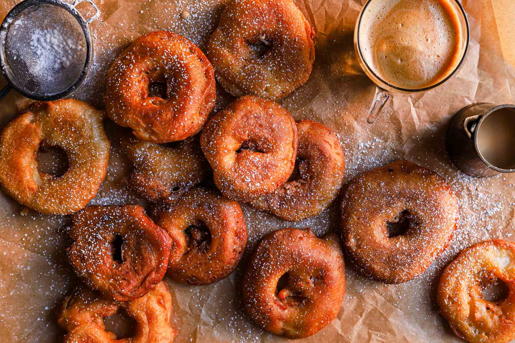 Homemade Apple Fritters are displayed on a table. The apple rings are fried golden in a cinnamon-spiced batter.