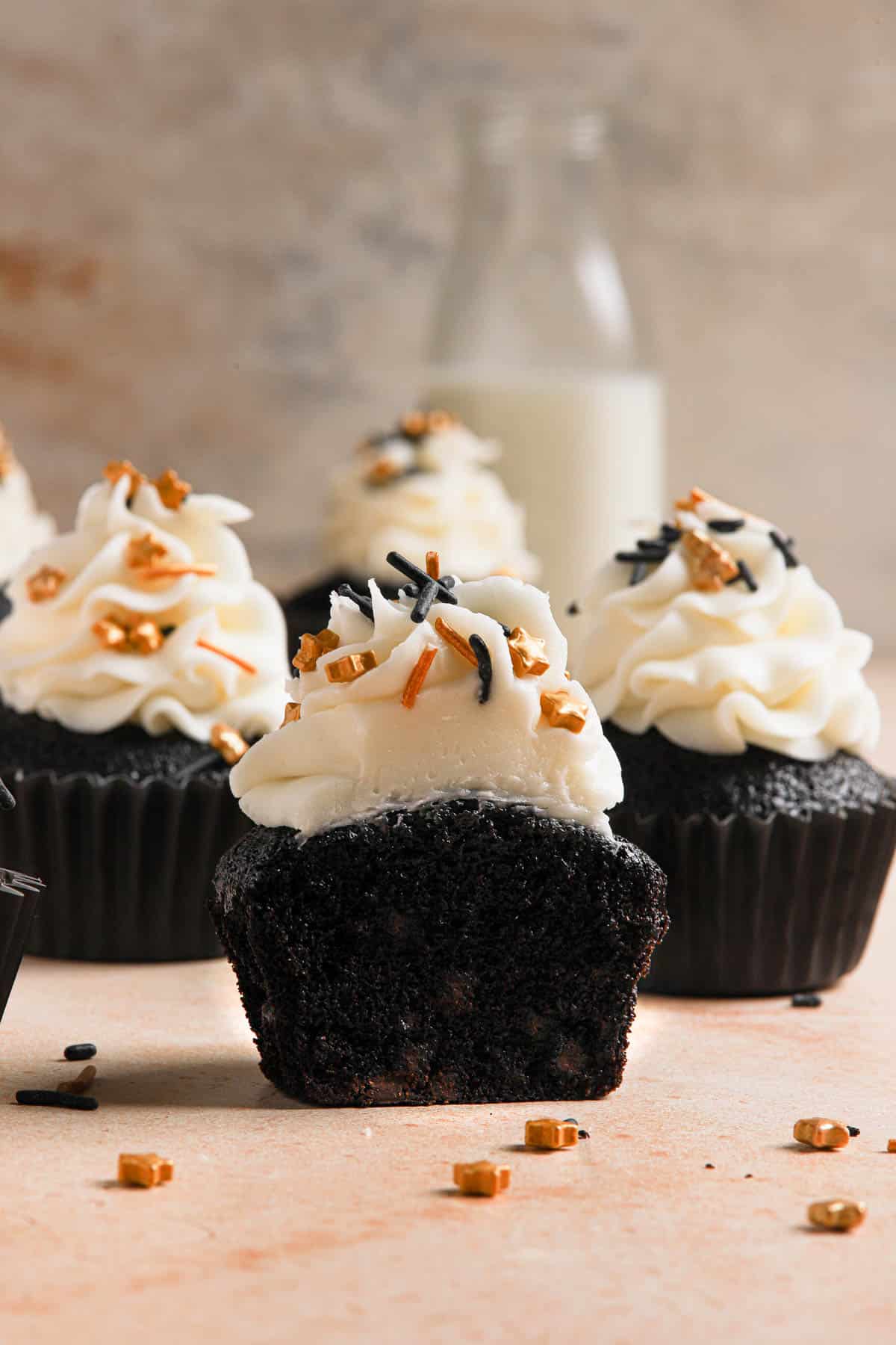 A close-up image of a black cocoa cupcake with a bite taken out of it shows the soft, tender, moist cupcake with chocolate chips baked throughout.