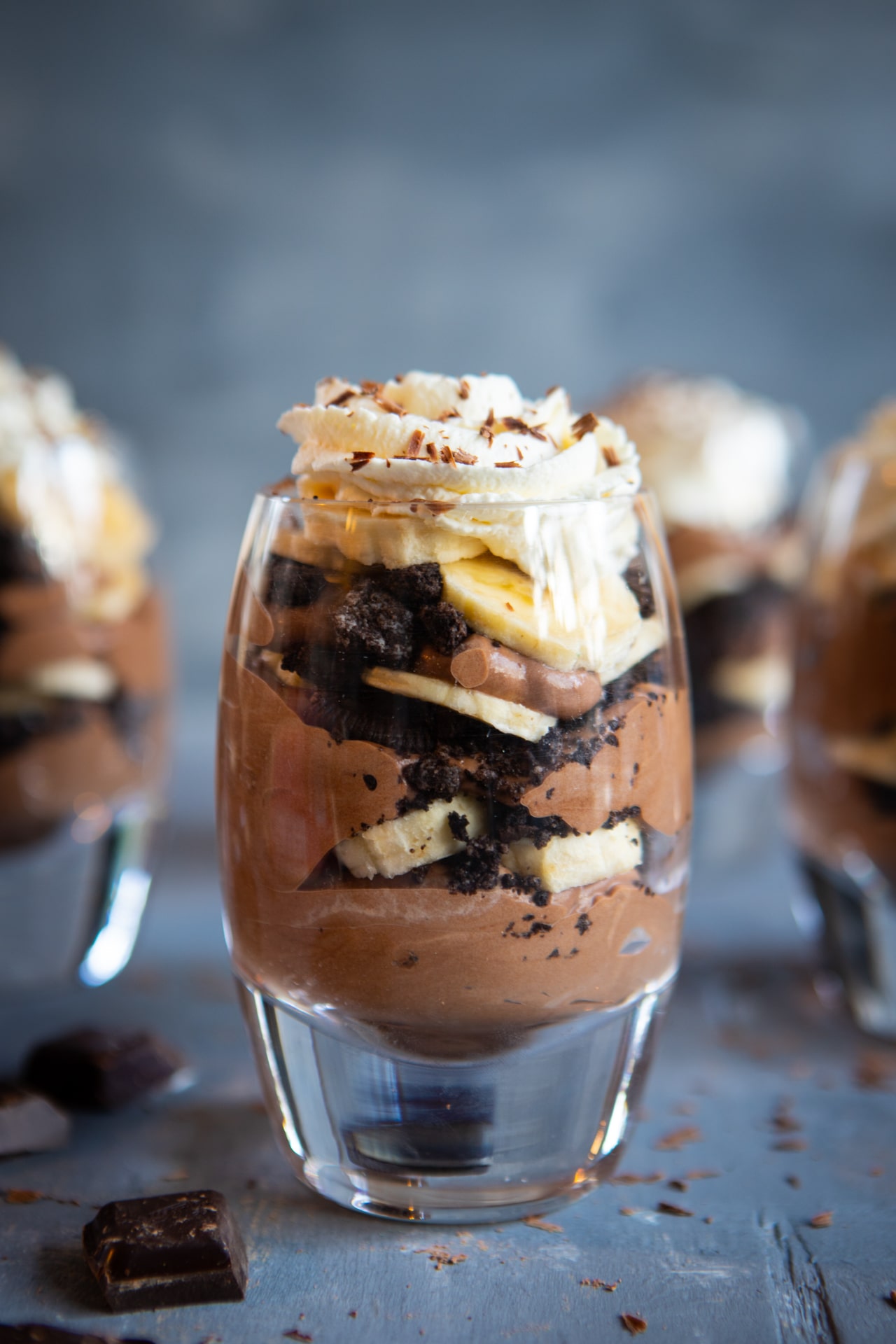 4 glasses of Chocolate Banana Pudding, with 3 in the background, blurry, and one in the foreground, in focus, so you can see all the beautiful layers of dessert.