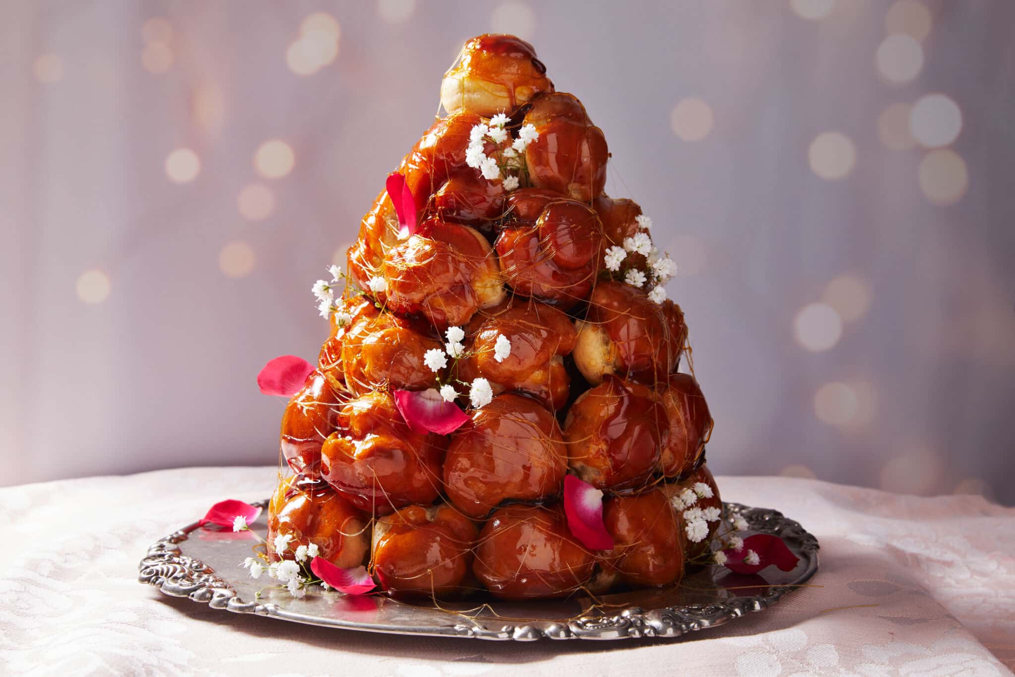 A tower of cream puffs glazed in caramel sauce, with floral decorations on a plate.