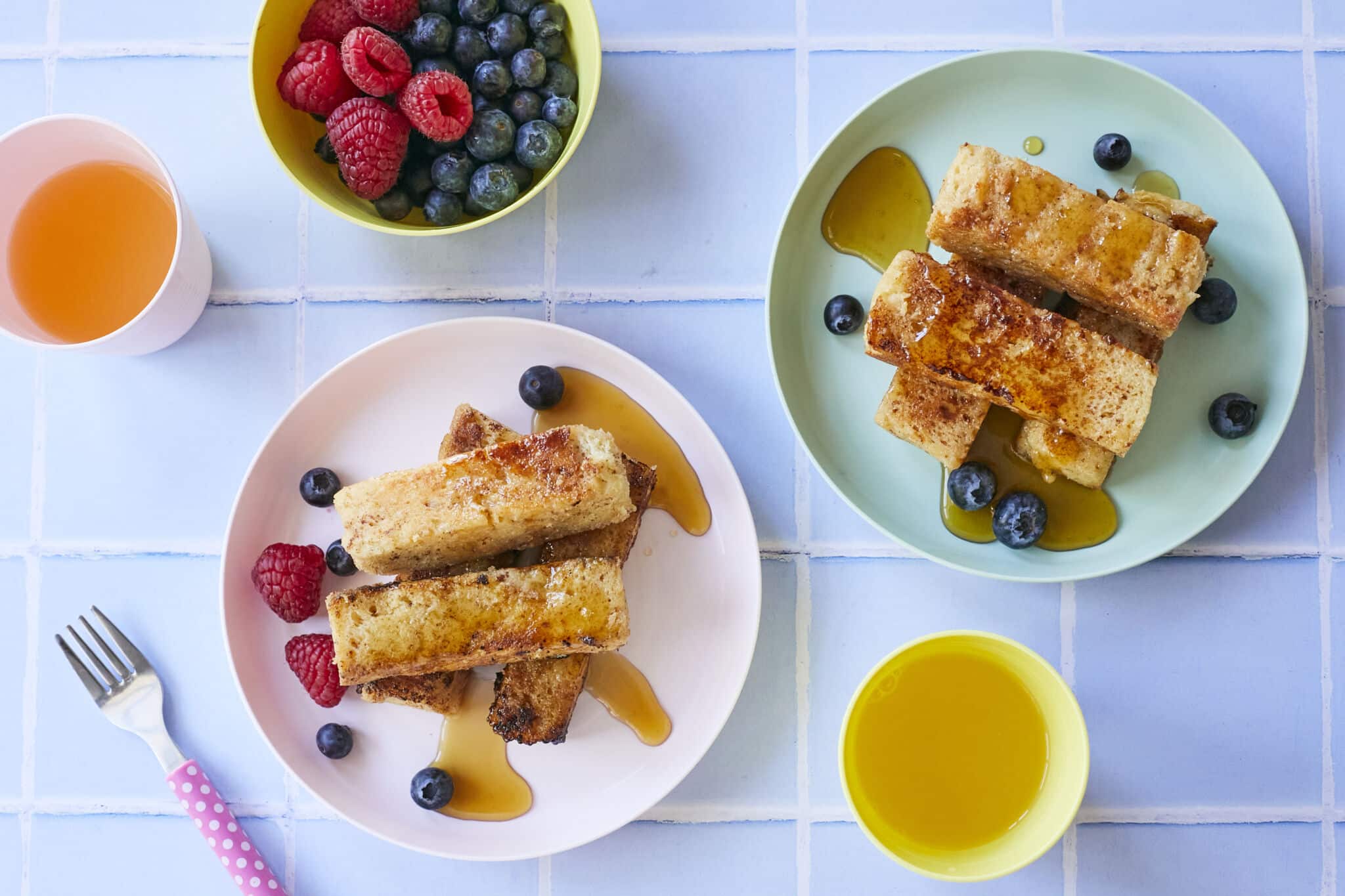 Golden brown French toast sticks paired with Fresh raspberries and blueberries, with syrup on the side.