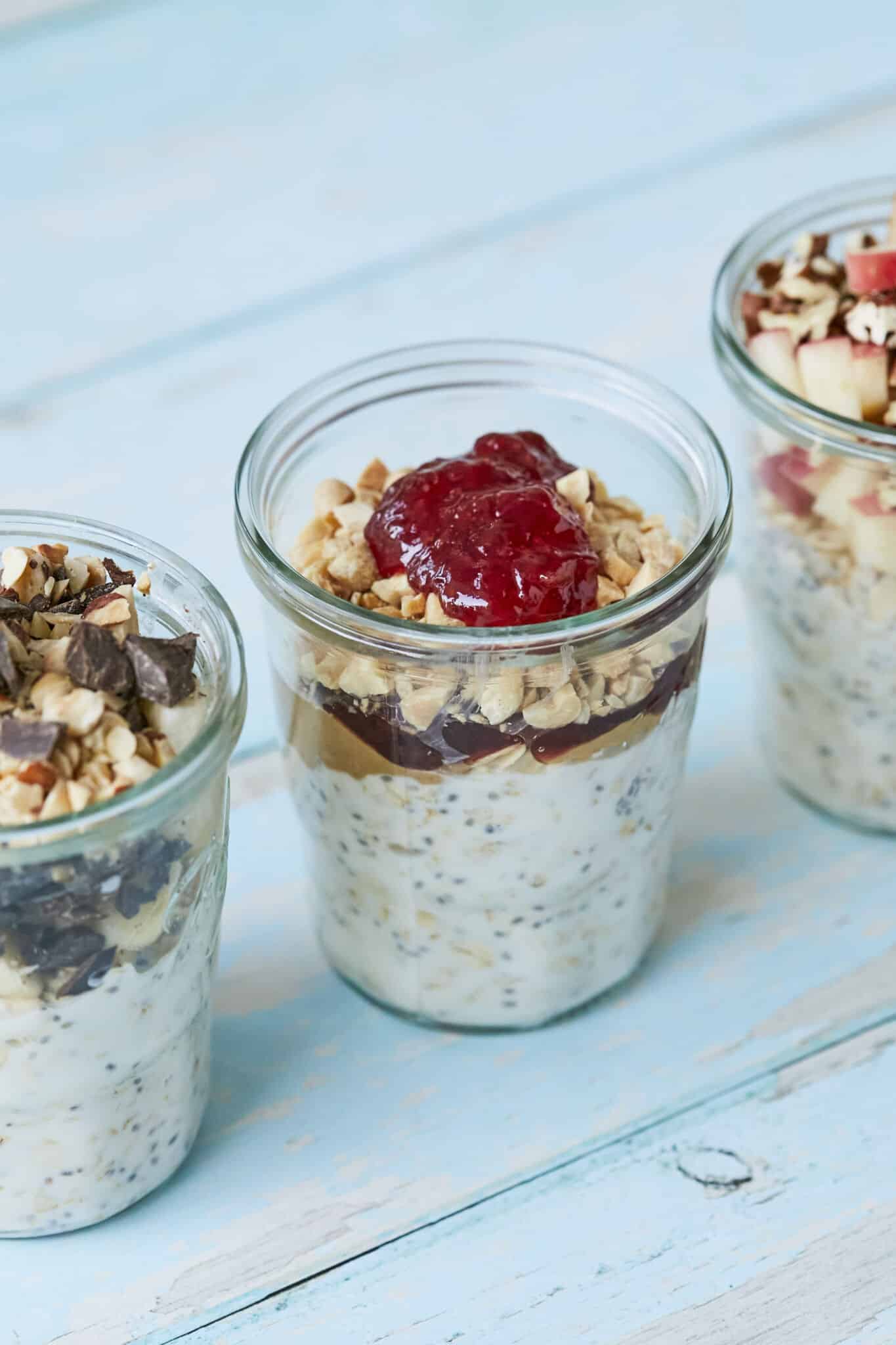An additional sideview of the 3 jars of Overnight Oats so you can see the layers of ingredients in glass jars on a blue wooden table.