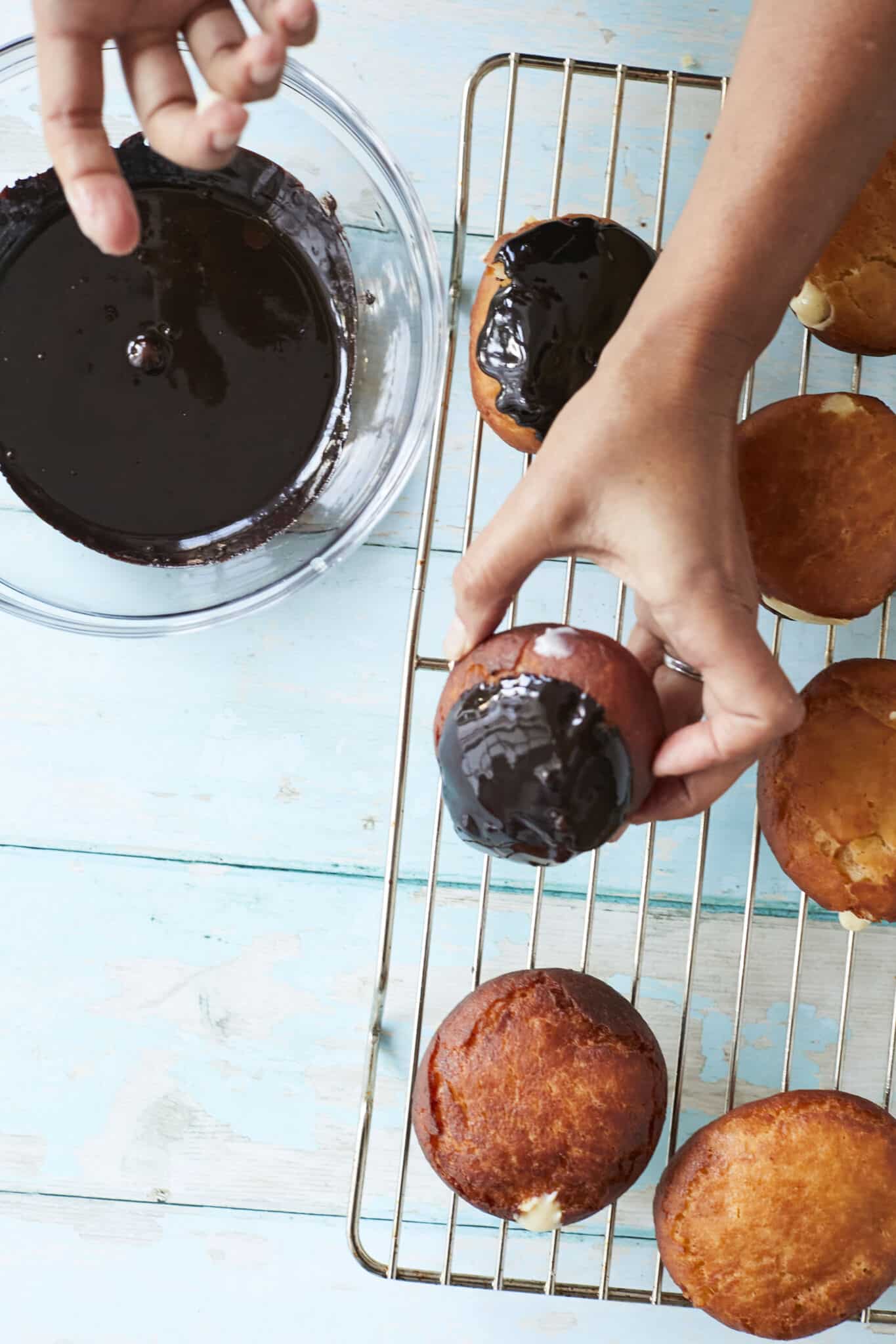 Adding chocolate glaze to Boston Cream Donuts and then placing them on a cooling rack.