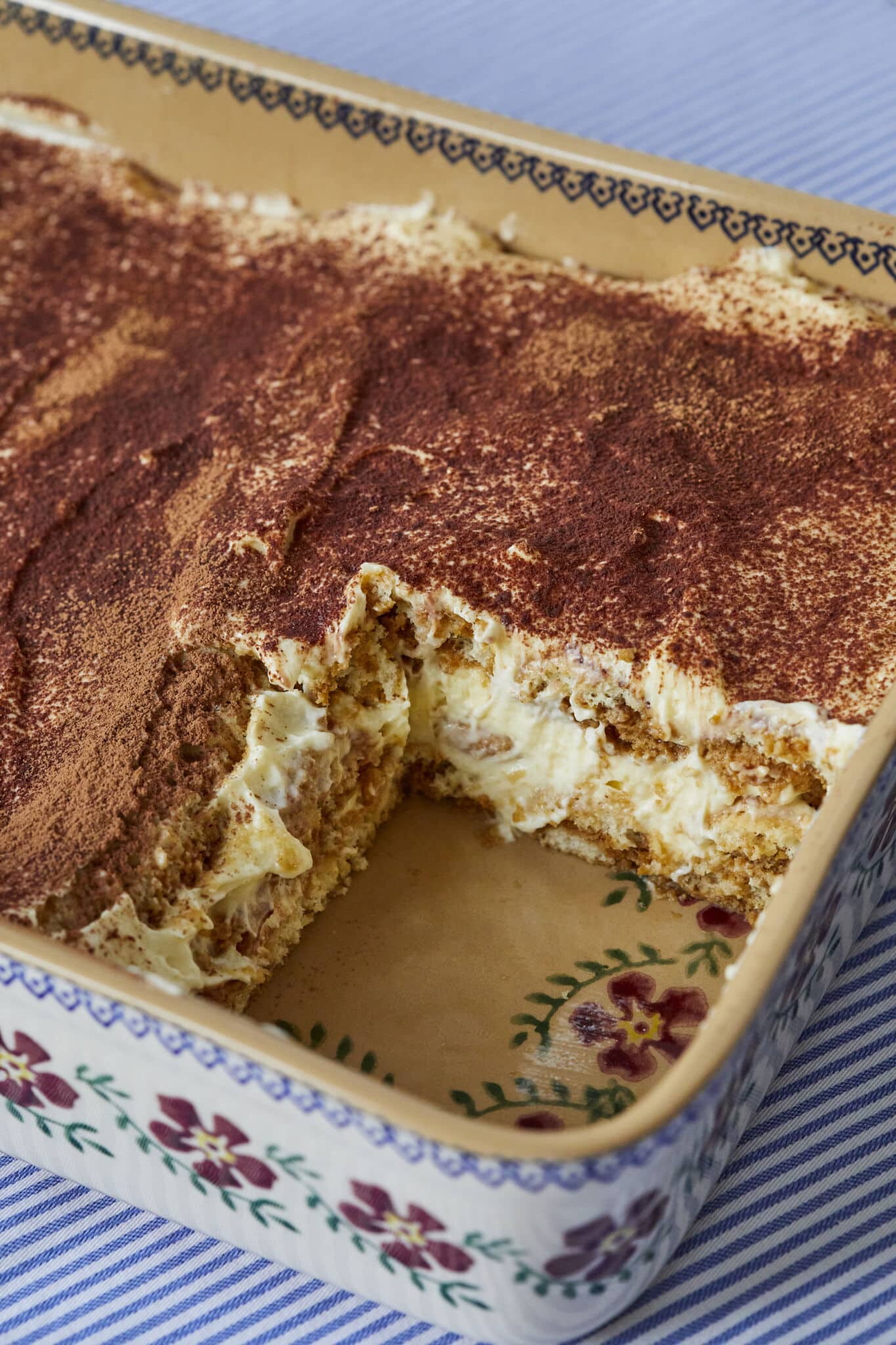 The Best Tiramisu recipe made 100% from scratch in a baking dish with one piece removed