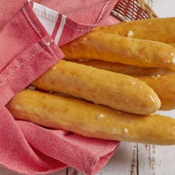 Baked golden breadsticks covered with rich garlic butter, wrapped with towel in a serving basket.