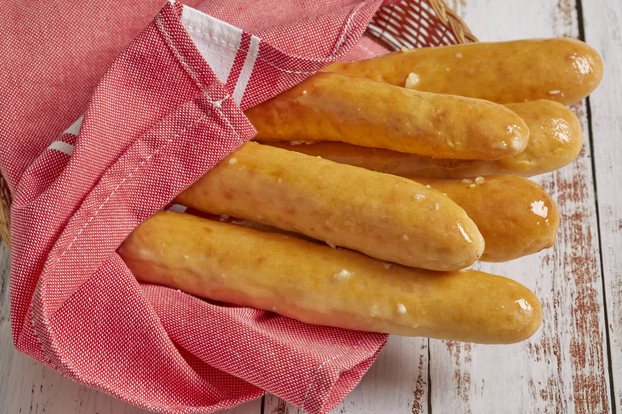 Baked golden breadsticks covered with rich garlic butter, wrapped with towel in a serving basket.