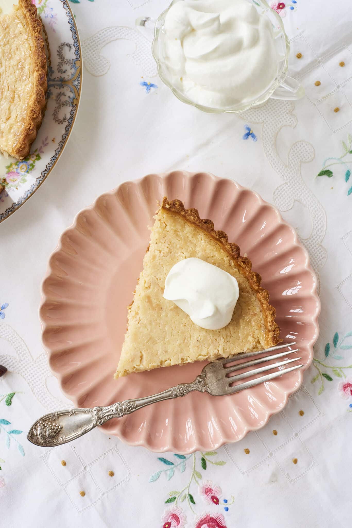 A slice of coconut custard tart on a plate served with a big dollop of whipped cream. 