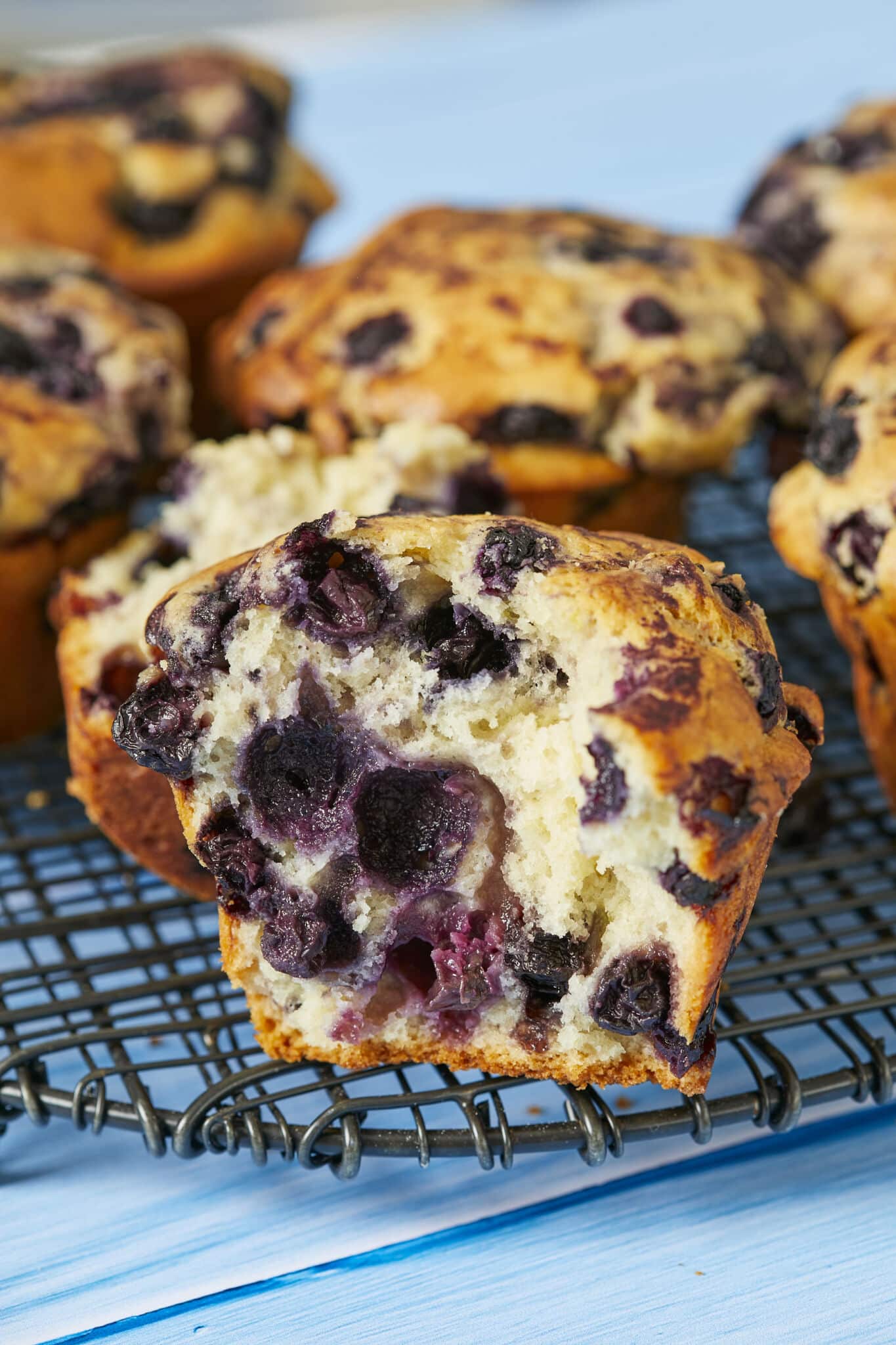 Half of a muffin in front loaded with juicy blueberries, showing the soft and bubbly tender inside. Other muffins are in the back.