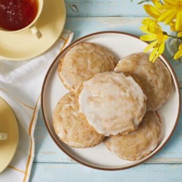 Baked Soft Lemon Cookies dipped with Zesty Lemon Glaze, served on a plate with tea on the side.