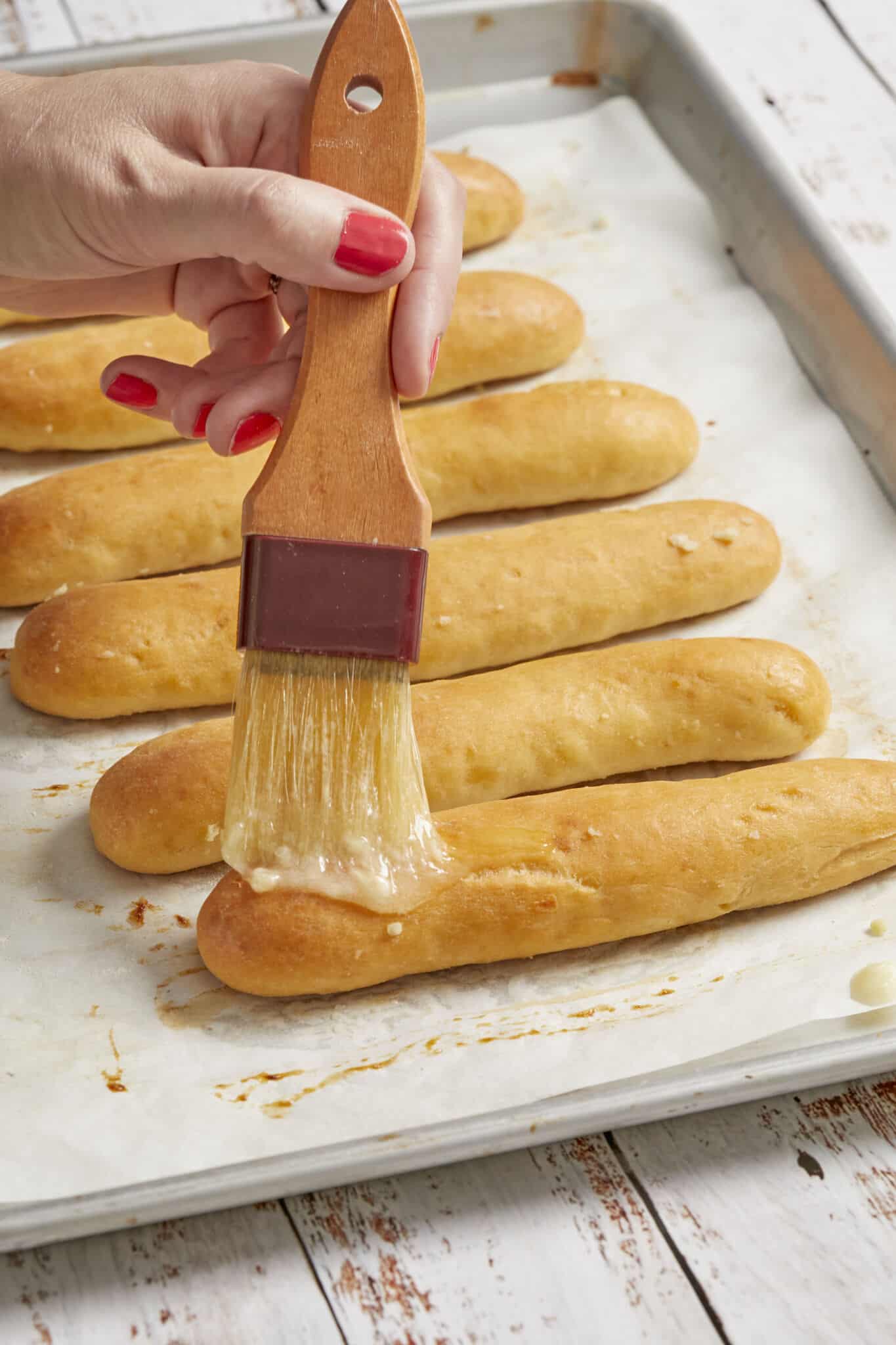 Brush garlic butter onto baked golden breadsticks on a baking tray. 