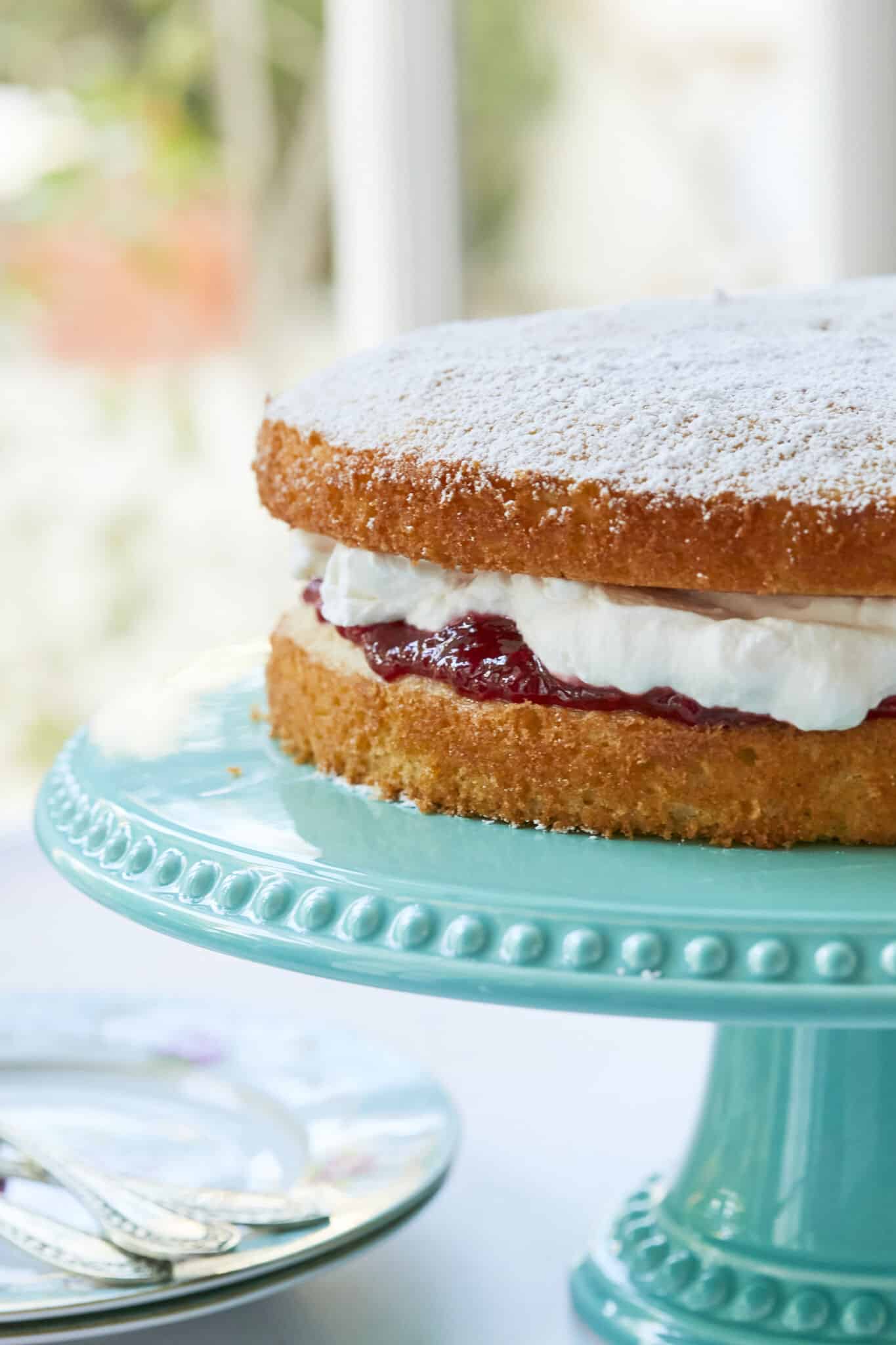 Classic Victoria Sponge Cake filled with freshly whipped cream, strawberry jam and dusted with powdered sugar. 