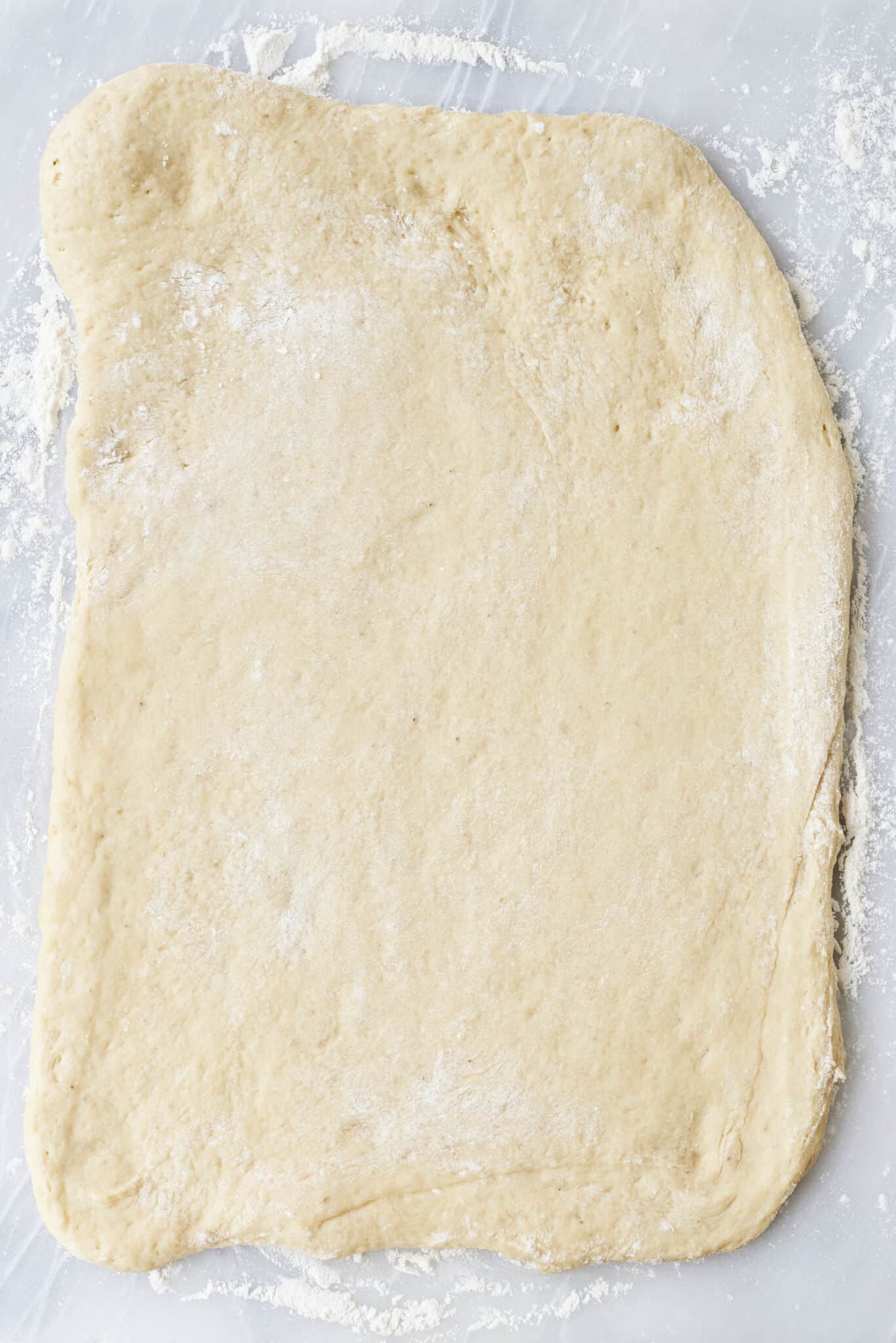 A well-proofed sofa dough is rolled into a rectangular shaped on the floured surface. 