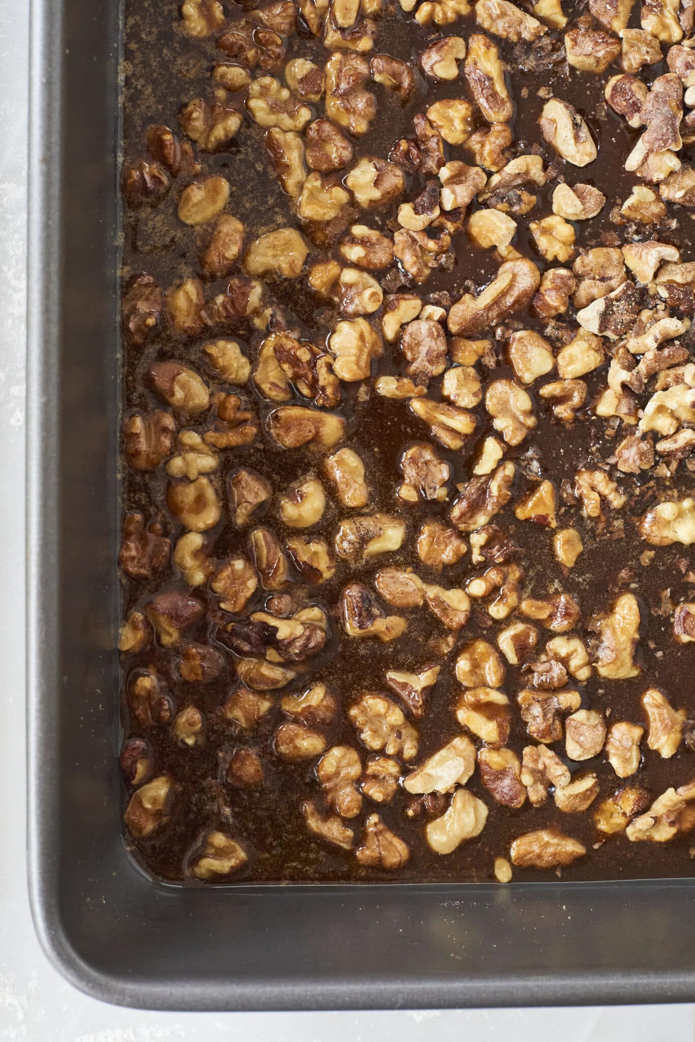 The rich caramel is in deep amber color and sitting in the prepared pan with toasted walnuts scattered on top. 