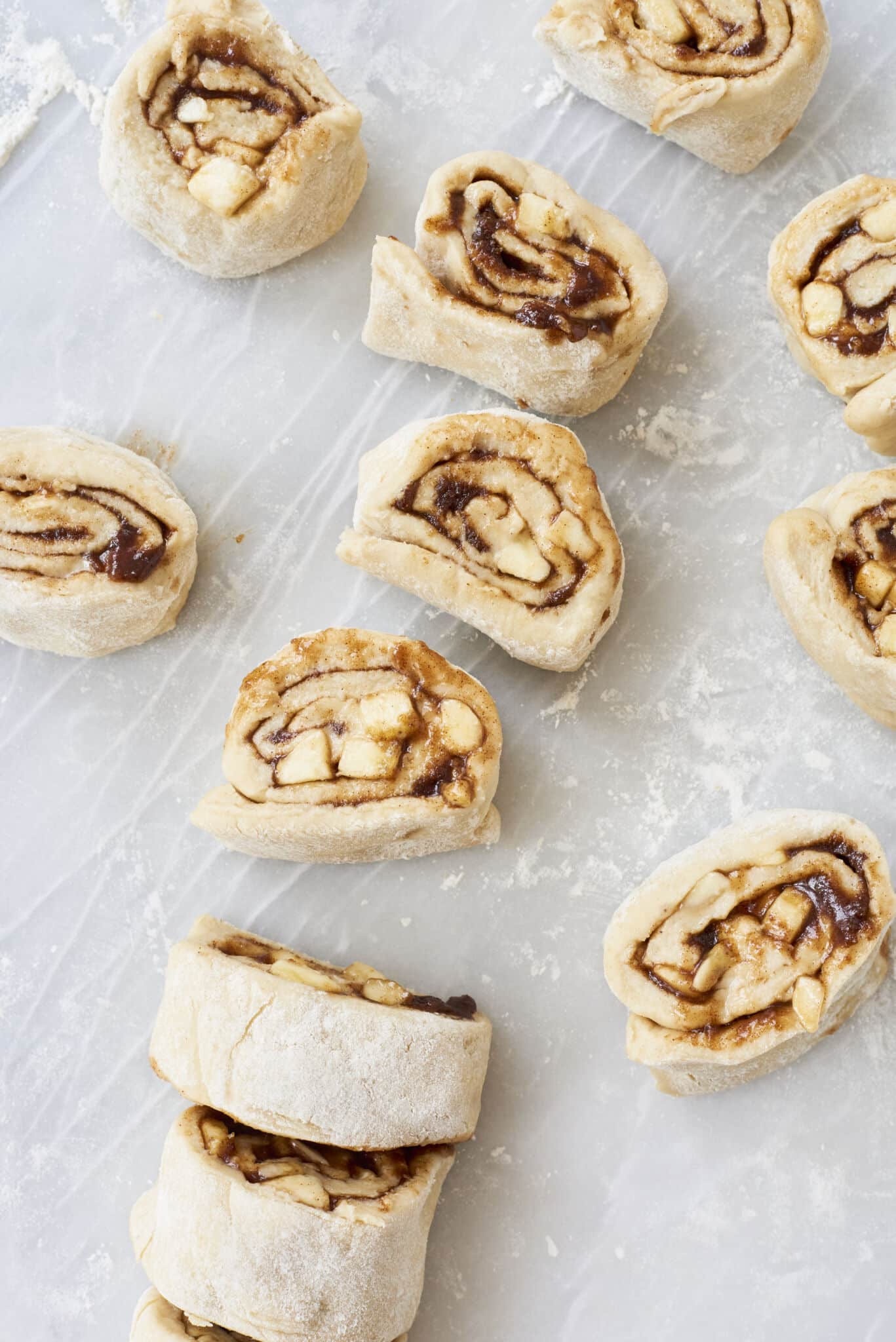 The equally-sized individual small logs are on a floured surface, with fresh bananas and gooey cinnamon sugar filling facing up. 