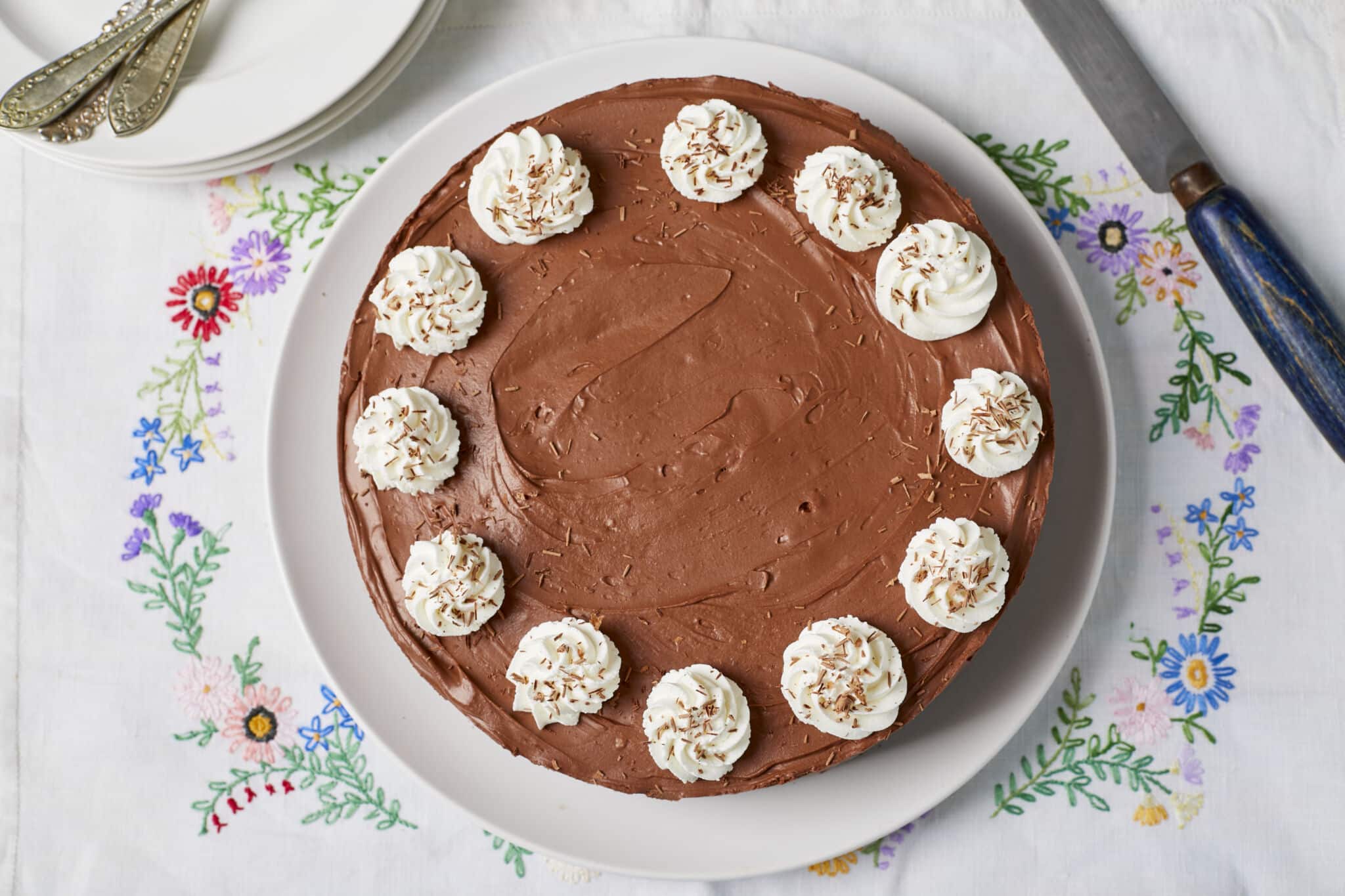 Extremely rich, decadent, and smooth No-Bake Chocolate Cheesecake is served on a white plate topped with whipped cream rosette and chocolate shavings.