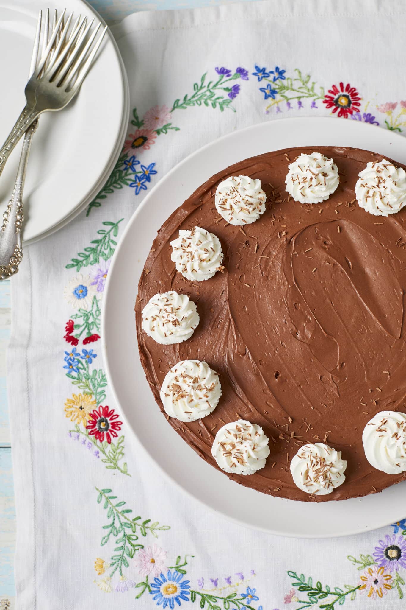 Extremely rich, decadent, and smooth No-Bake Chocolate Cheesecake is served on a white plate topped with whipped cream rosette and chocolate shavings.