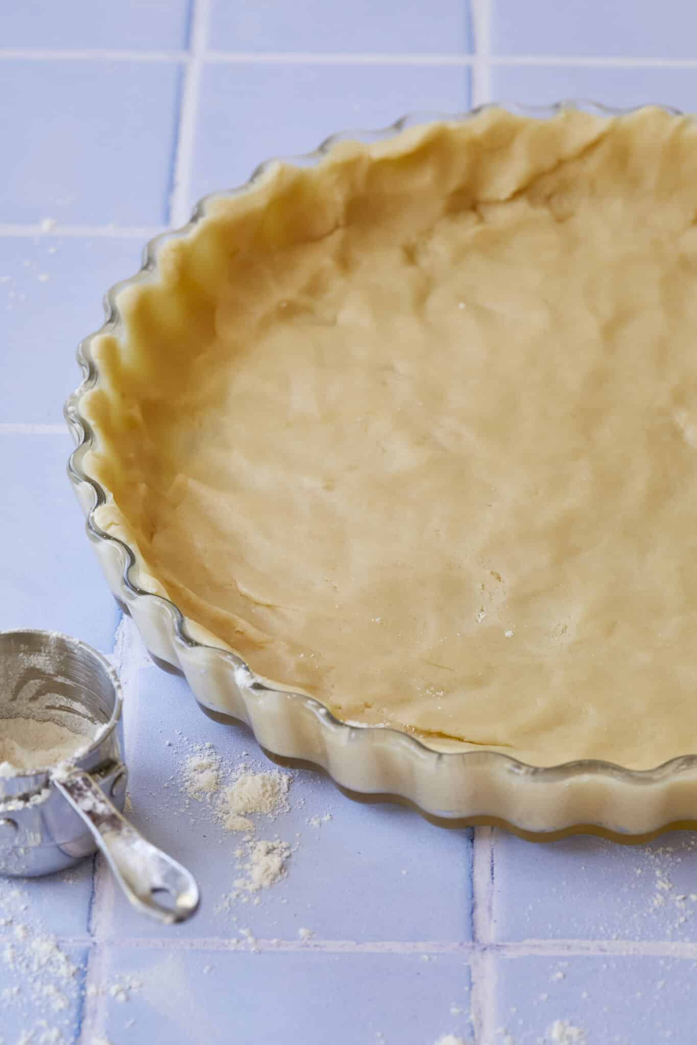 Pâte Sucrée pastry is pressed into a tart dish with dusting flour on the side