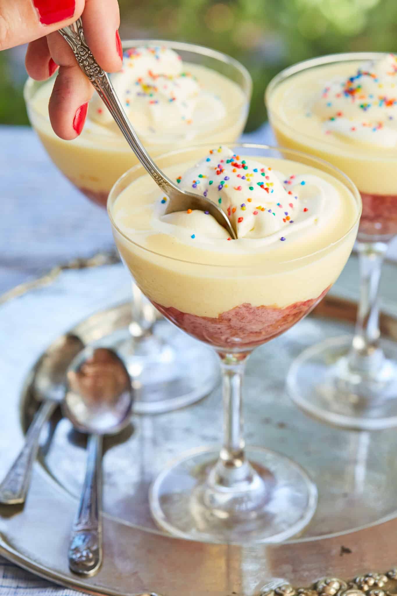 A spoon is scooping the Traditional English Trifle from the top through aerated whipped cream, velvety creme anglaise, then to the bottom of fruity jelly and boozy moist pound cake. 